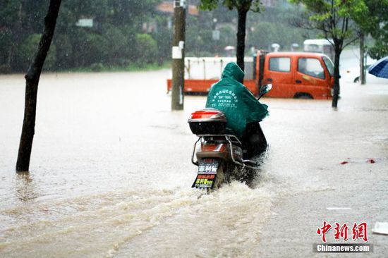 6月19日，江西省景德镇市遭遇暴雨袭击，导致城区部分小区和道路积水严重，市民出行不便。图为市民冒雨在江西省景德镇市朝阳路积水路段骑行。