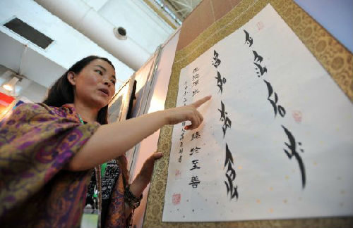 资料图片：2013年9月7日，在第四届中国桂林国际旅游博览会上，一名来自湖南省江永县的女子在推介一幅女书艺术作品。新华社记者陆波岸摄