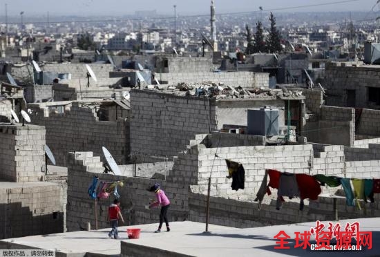 资料图：图为叙利亚当地孩子们在屋顶上晾衣服。他们身后，是大马士革饱受战火摧残的城区。