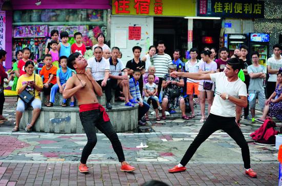 2017年7月8日，在白石洲股份 公司附近，两名民间艺人在表 演“钢筋绕脖”绝艺。图/IC