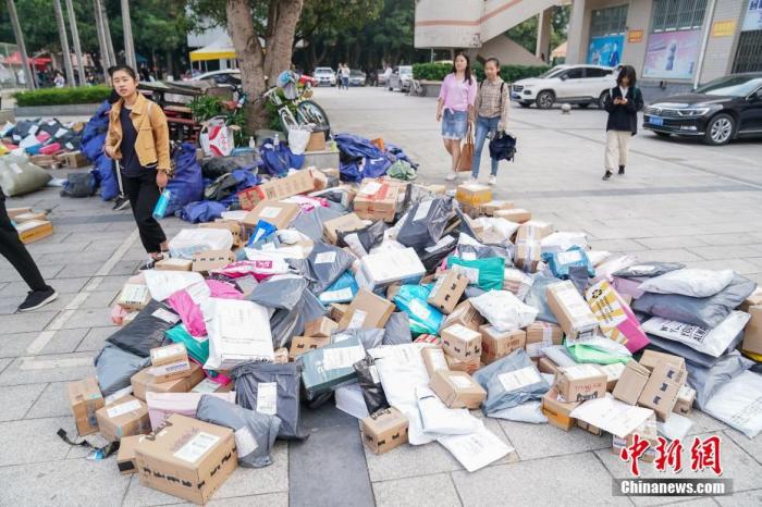 资料图：广西大学东校园菜鸟驿站外，学生从一批刚卸车的快递前路过。中新社记者 陈冠言 摄