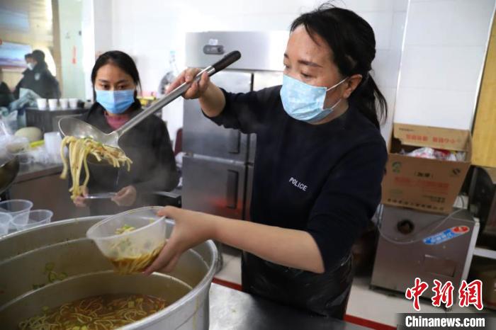 图为女干警在食堂做饭，并将做好的面食装进餐盒中。 玛多县委宣传部 摄