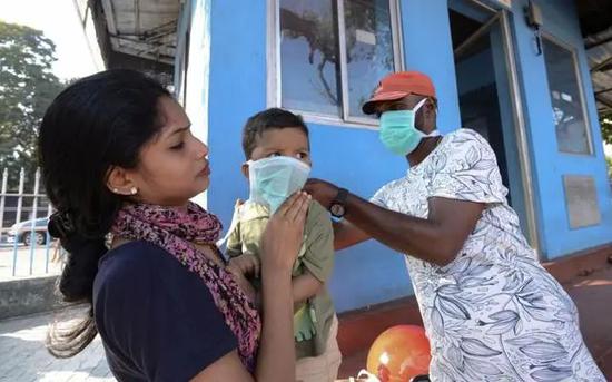 △印度南部喀拉拉邦某医院外，一名男性正在帮一个孩子戴口罩（图源：AP）