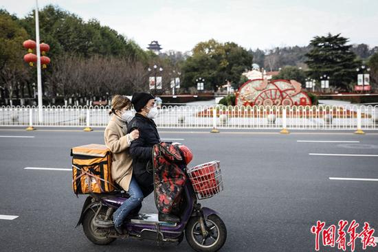 2月29日，武汉市，一对年轻男女驾驶着送外卖的电动车驶过。中青报·中青网记者 赵迪/摄