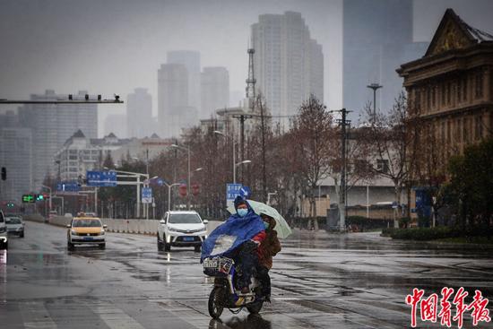 2月15日，武汉市，两位市民坐在电动车上冒雪驶过空荡荡的城市。